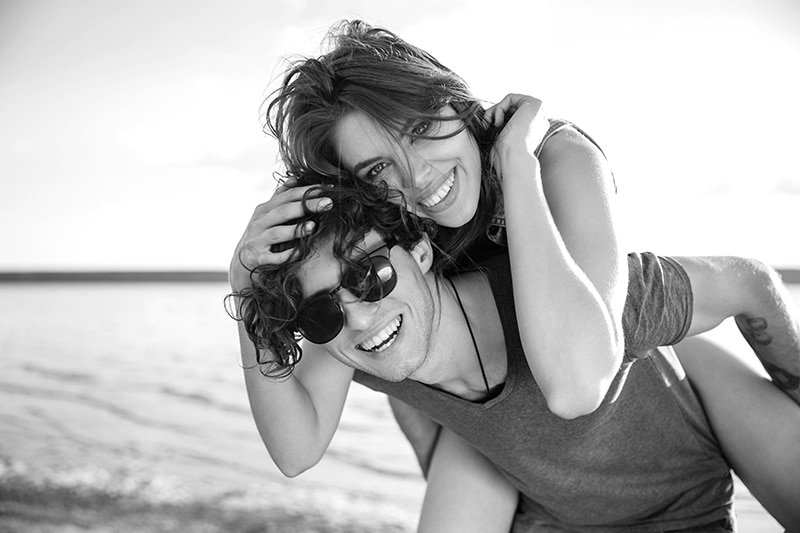 Man giving piggyback ride to girlfriend by the ocean
